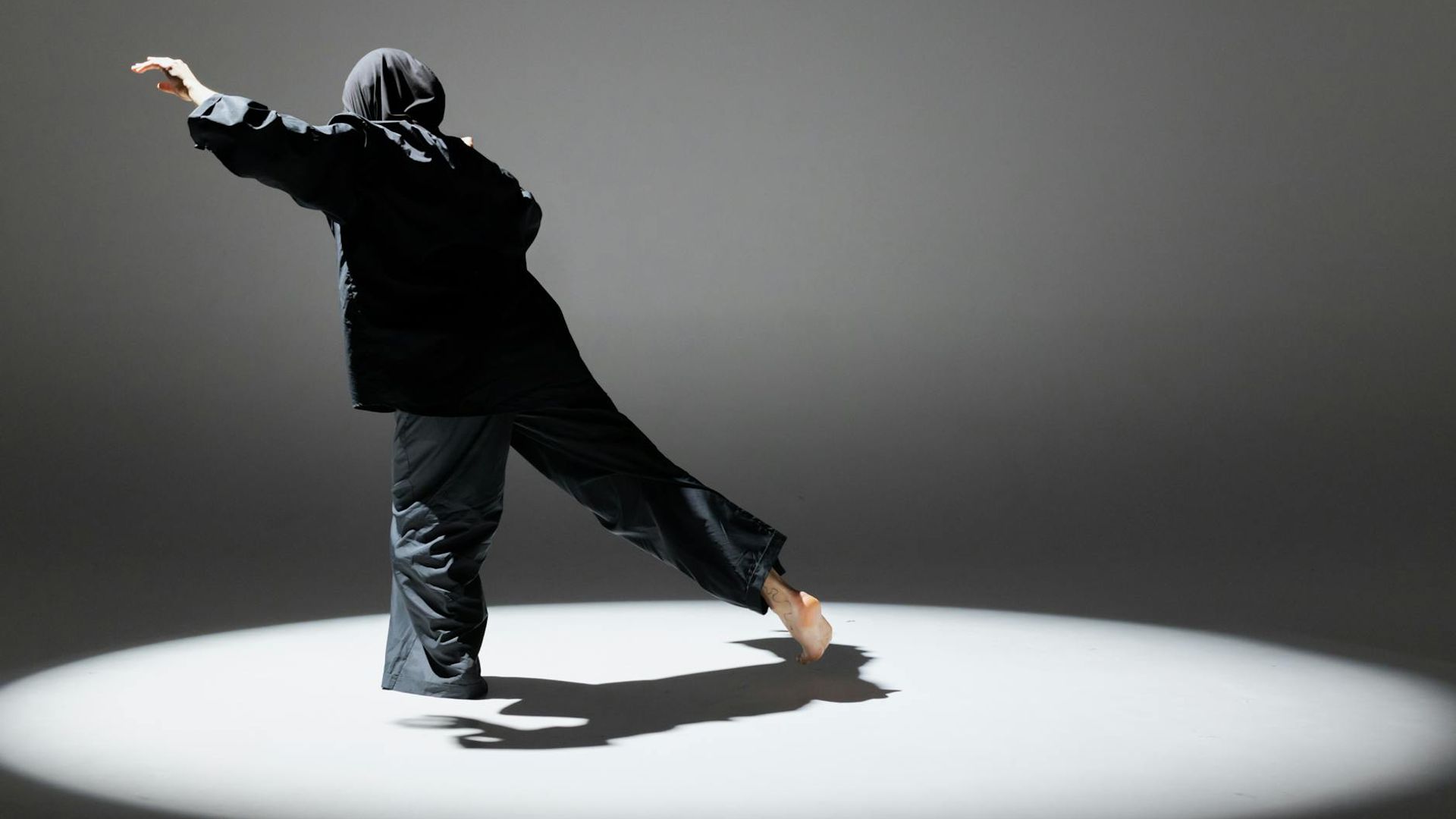 A person in silhouette performing dynamic movements in a dark studio